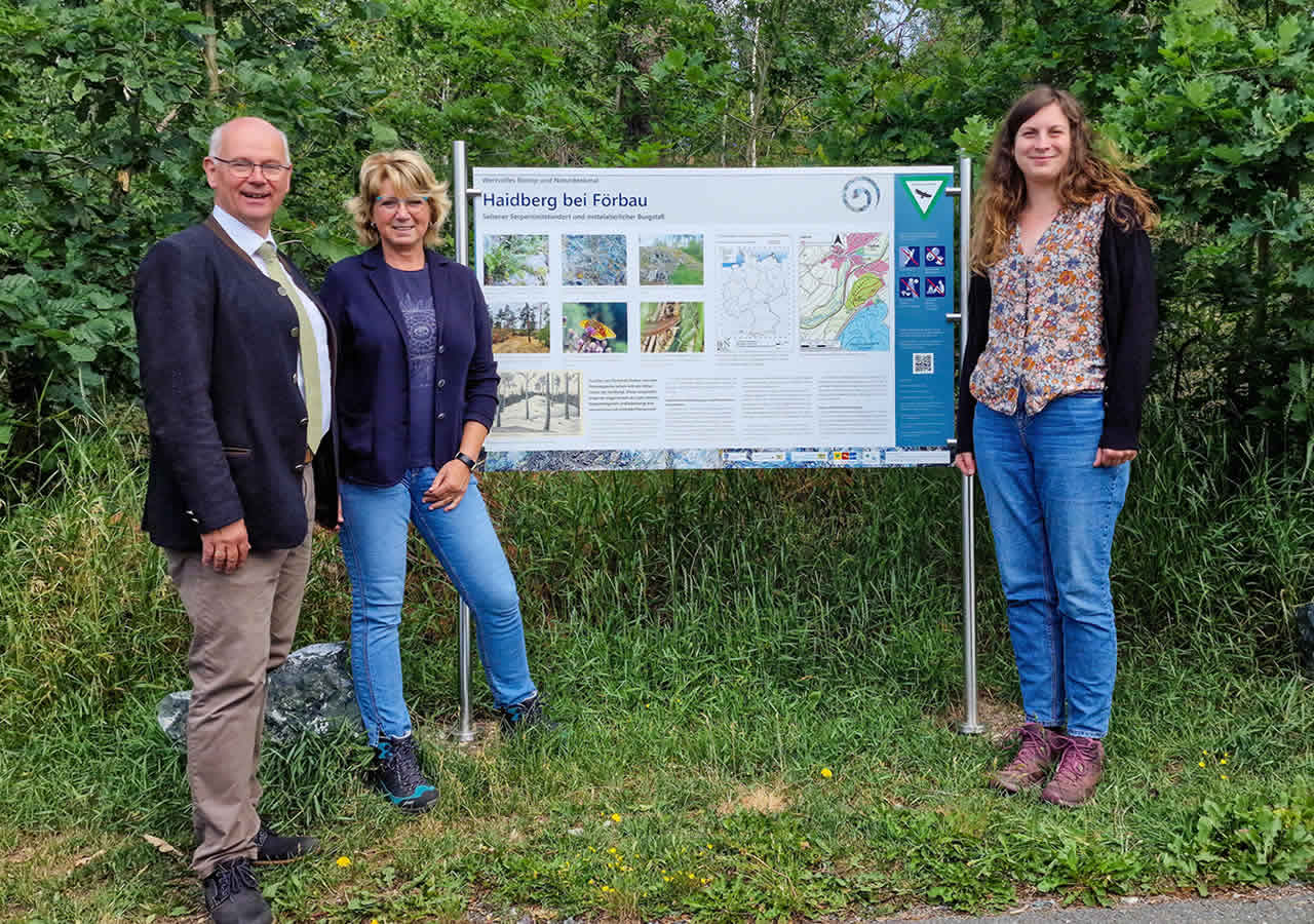 Bürgermeister Hans-Peter Baumann und die Mitarbeiterinnen des LPV, Regina Saller und Isabel Kaske, am neu aufgestellten Infoschild zum Haidberg bei Förbau.